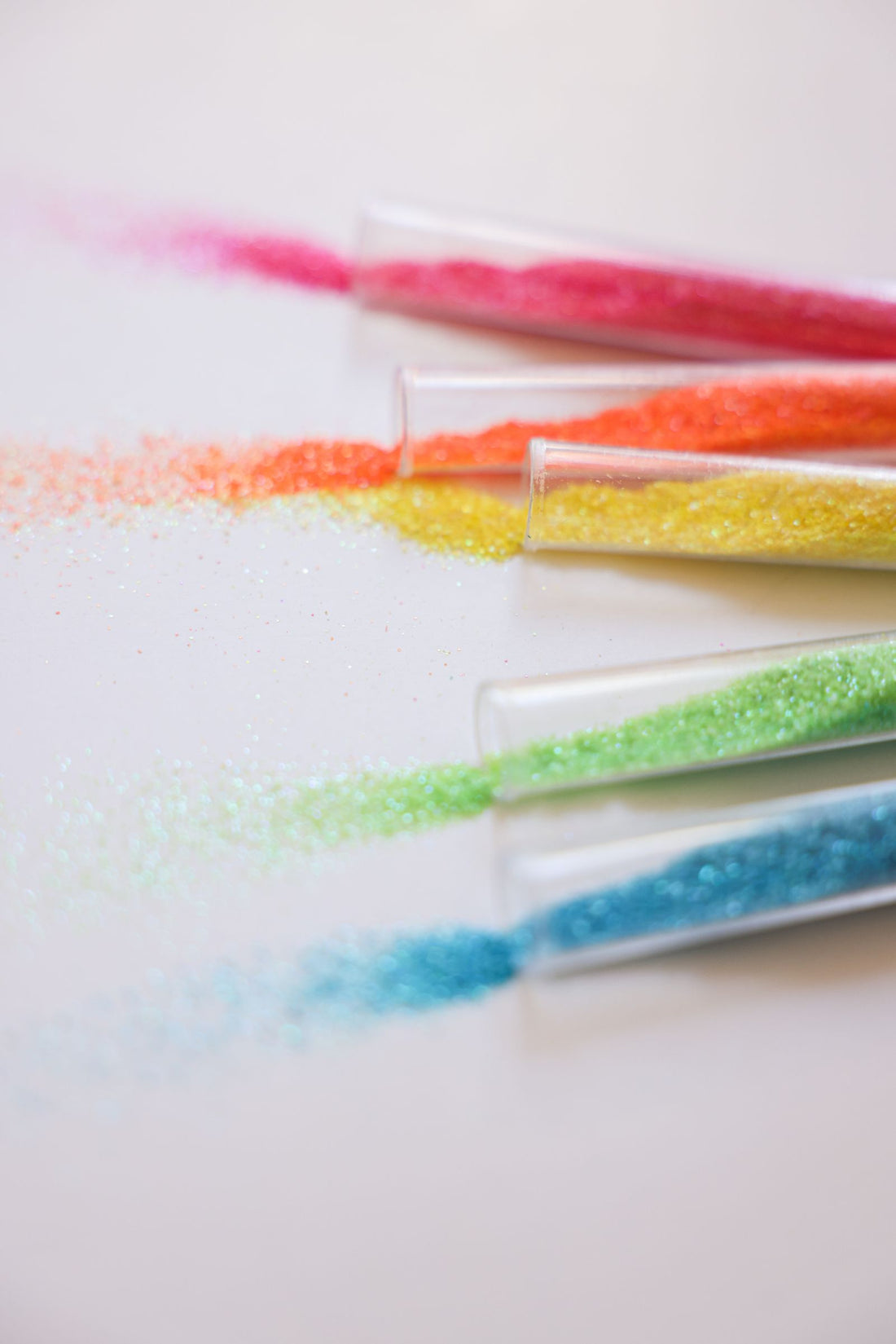 Poudres colorées nacrées répandues devant des tubes sur un fond blanc