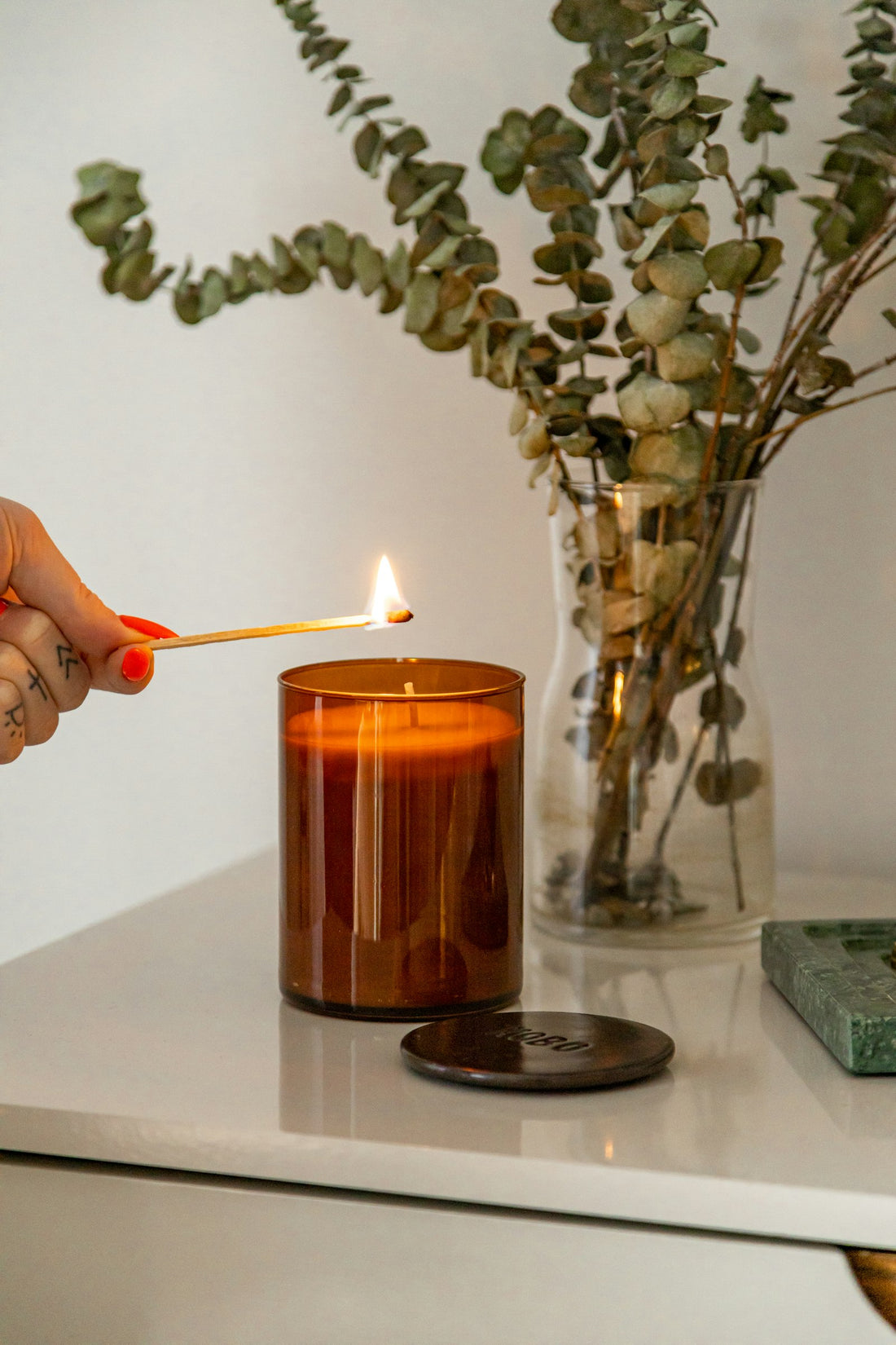 Main allumant une bougie dans un pot en verre brun avec une allumette