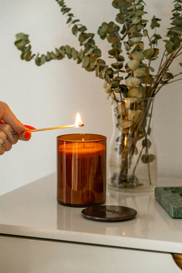 Main allumant une bougie dans un pot en verre brun avec une allumette