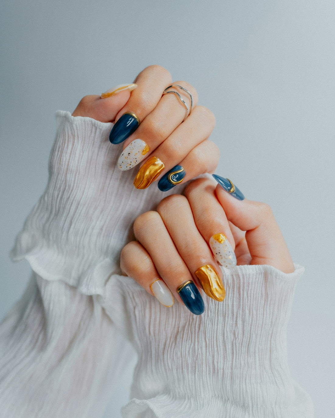 Mains de femme avec un nail art bleu marine, doré et blanc à effet paillueté